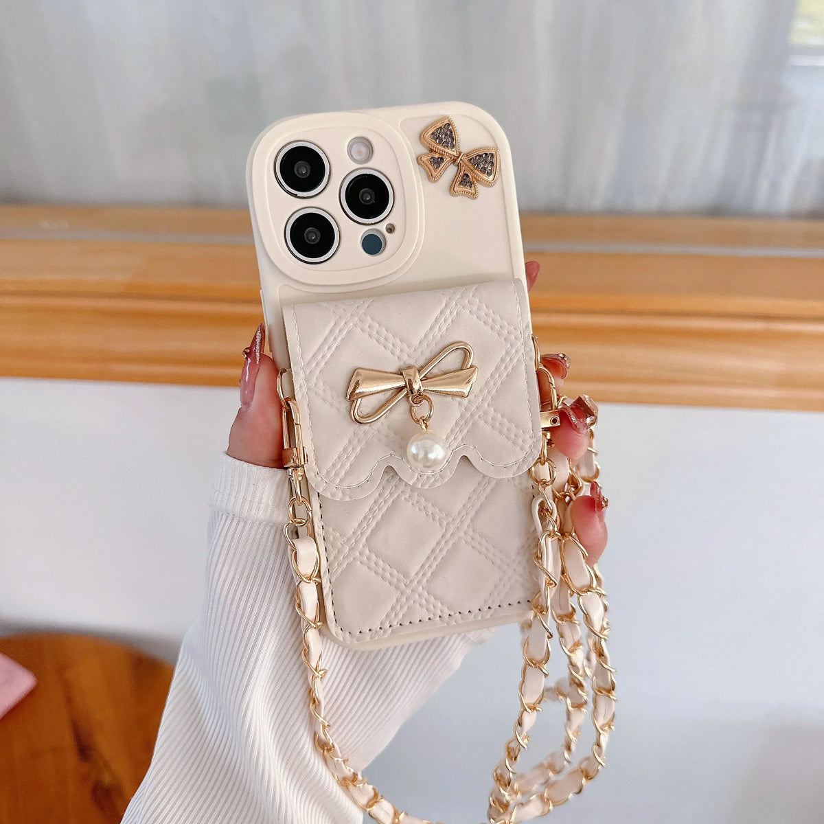 Phone case with bow design and chain strap held by a hand