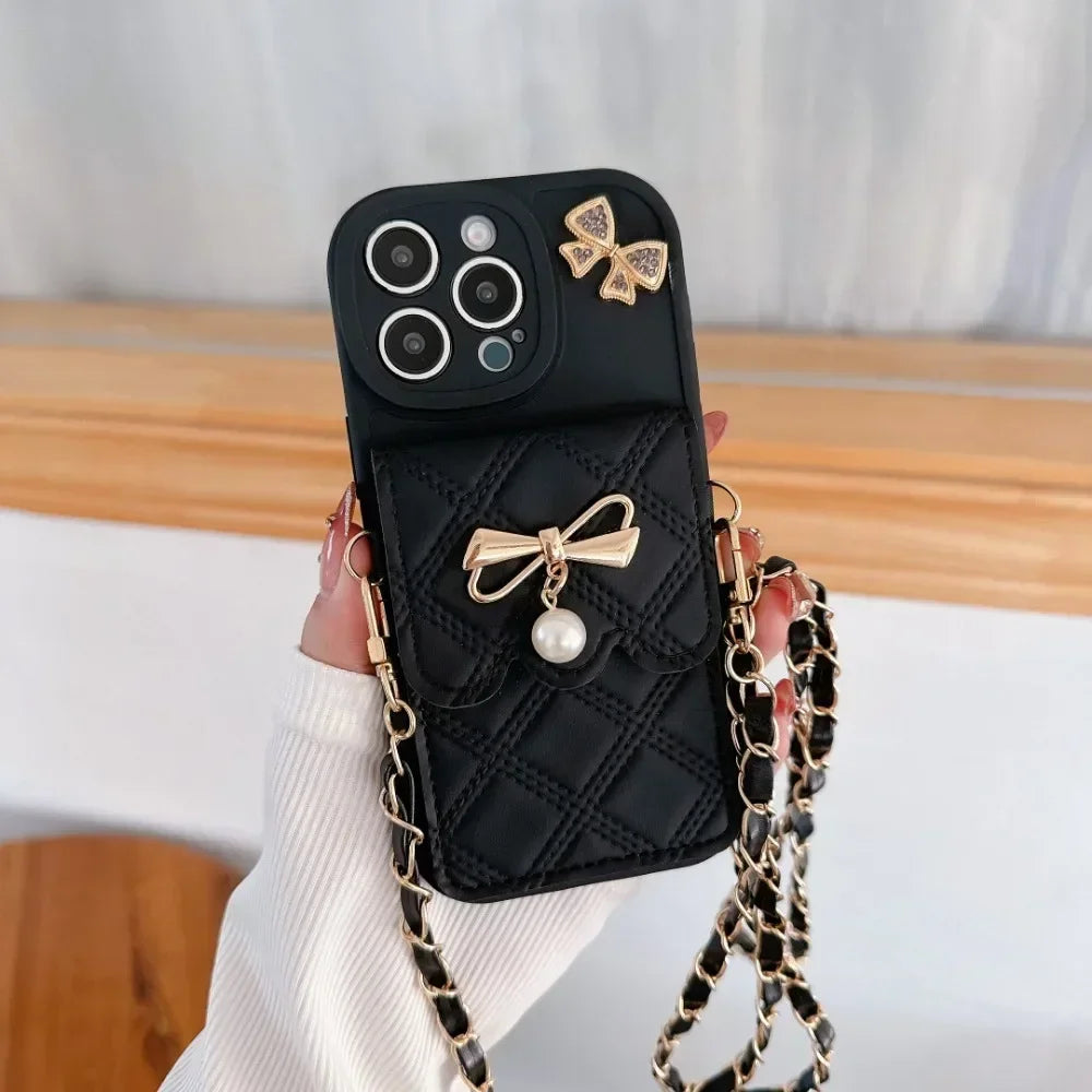Black phone case with gold bows and a chain strap held by a hand.