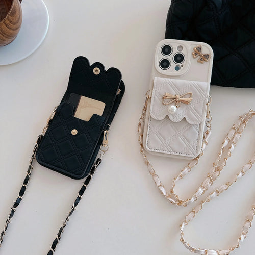 Two quilted phone wallet cases with chain straps are displayed on a light surface. One case is black with gold hardware and a black-and-white chain strap, and the other is white with gold hardware and a white-and-gold chain strap.